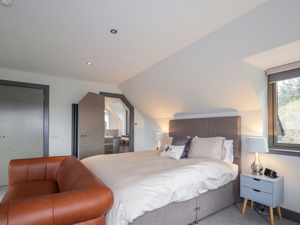 A bedroom with a gray bed a brown leather chair and a blue bedside table with a lamp at Ben Luna Lodge in Drumnadrochit Loch Ness
