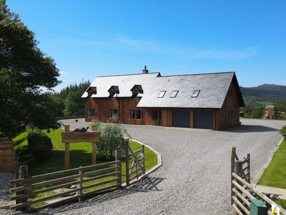 A wooden lodge with a gravel driveway and wooden gates at Ben Luna Lodge in Drumnadrochit Loch Ness