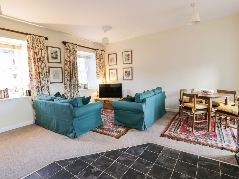 A living room with two teal sofas a wooden dining table with chairs and floral curtains at The Stables in Dalswinton