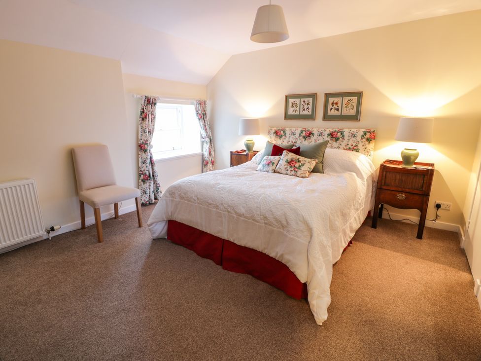 A bedroom with a double bed floral headboard bedside tables with lamps a chair and floral curtains at The Stables in Dalswinton
