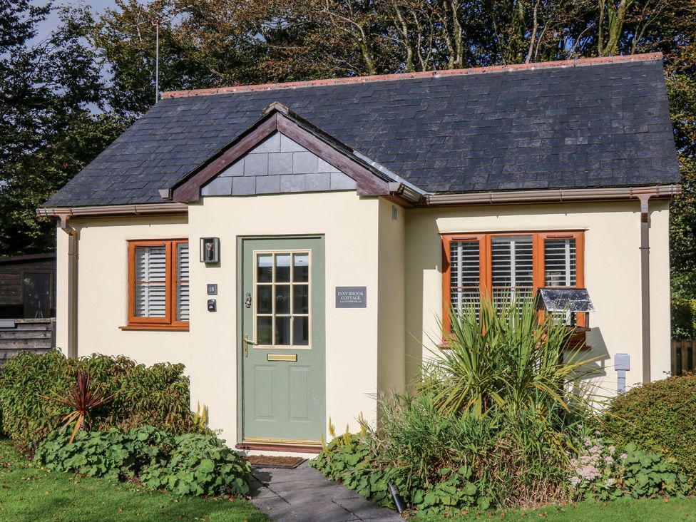 A small cottage with a green door flanked by two windows and surrounded by plants at Inny Brook Cottage in Davidstow near Camelford