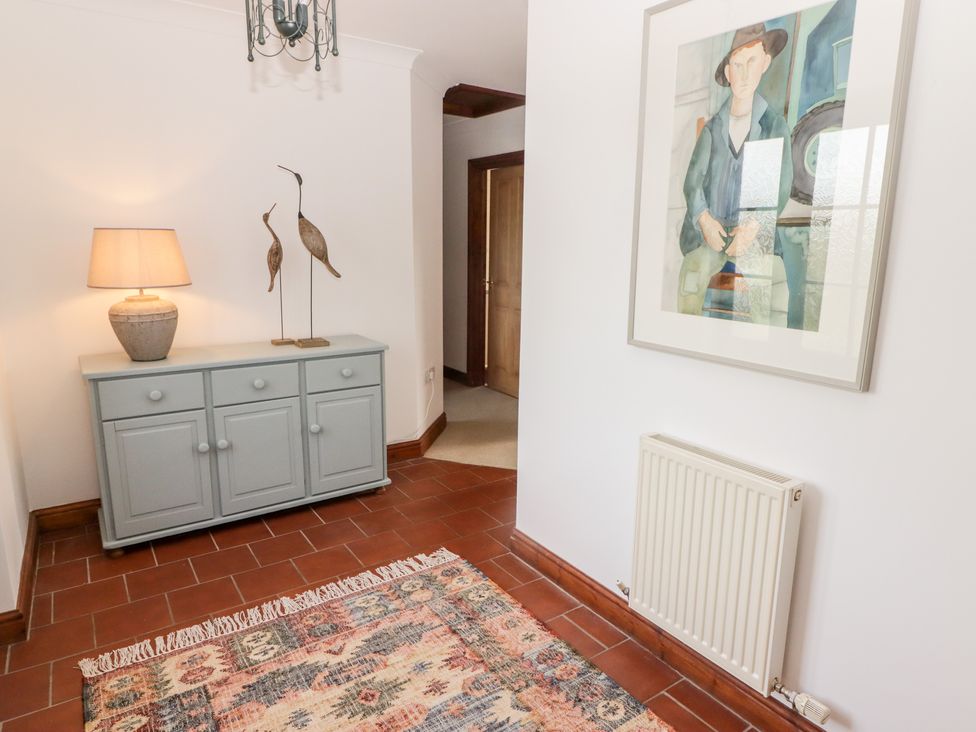 A hallway with a gray cabinet holding a lamp and bird sculptures a radiator on the wall and a framed painting at Fountain Folly in Moylgrove near St Dogmaels