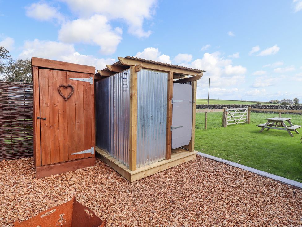 An outdoor area with a wooden shed, a corrugated metal structure, a wooden fence, and a picnic table on grass at The Black Sheep in Whithorn