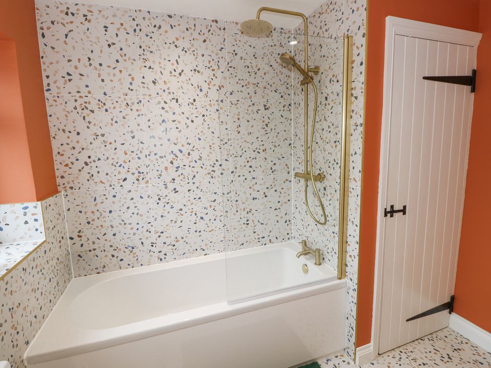 A bathroom with a bathtub shower combination with terrazzo tiles and orange walls at Frosthill Cottage in Carisbrooke