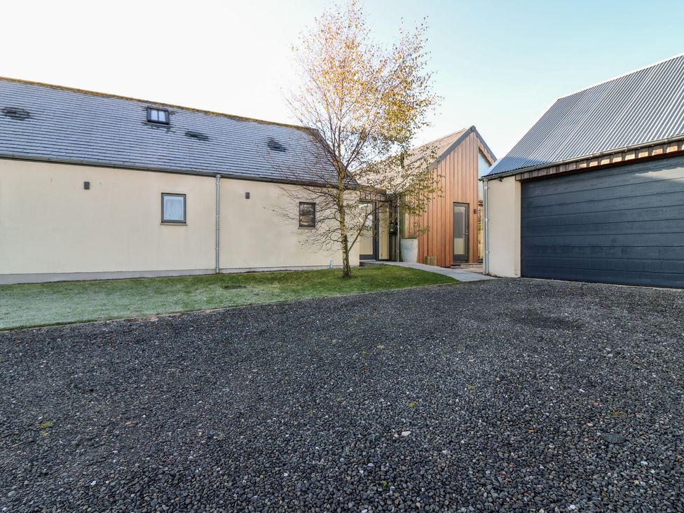 A gravel driveway with a tree a garage and a building with a slate roof and wooden entrance at The Lodge in Dunecht near Westhill