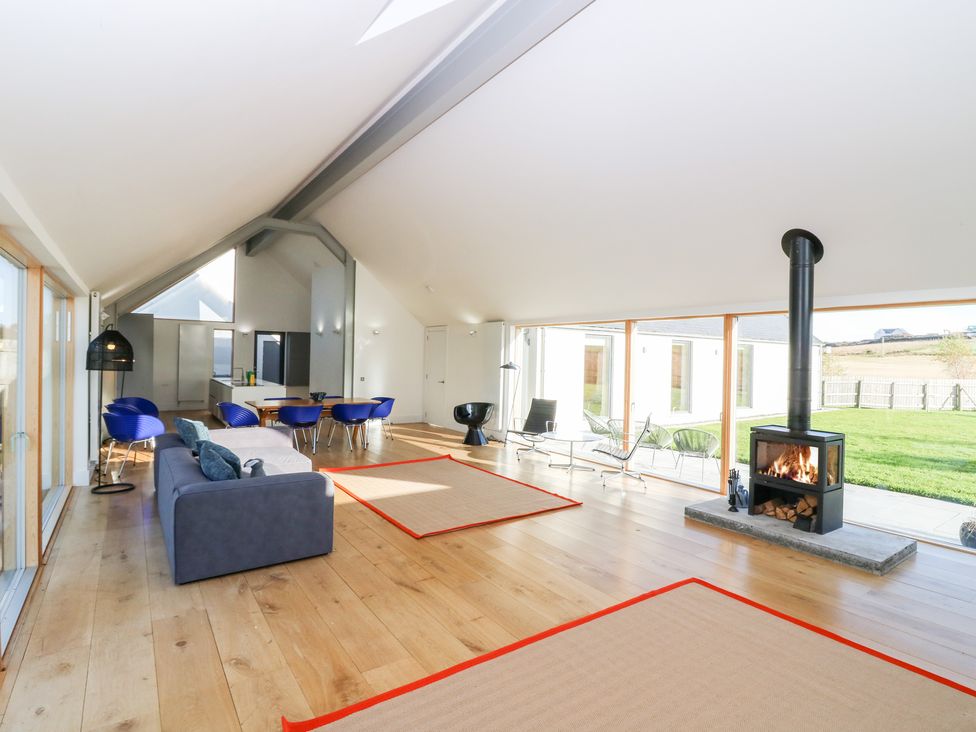 An open living space with a sofa and dining table with blue chairs next to large windows and a wood stove at The Lodge in Dunecht near Westhill