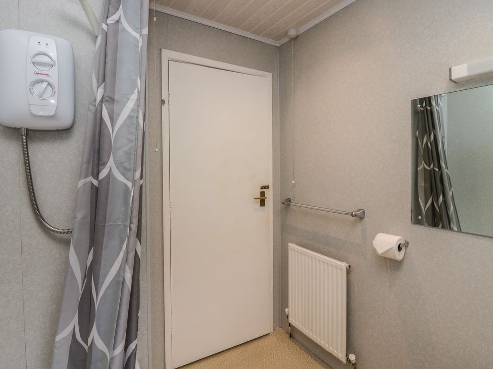 A bathroom corner with a closed door radiator towel rail toilet paper holder and mirror at Apartment 6 in Keswick