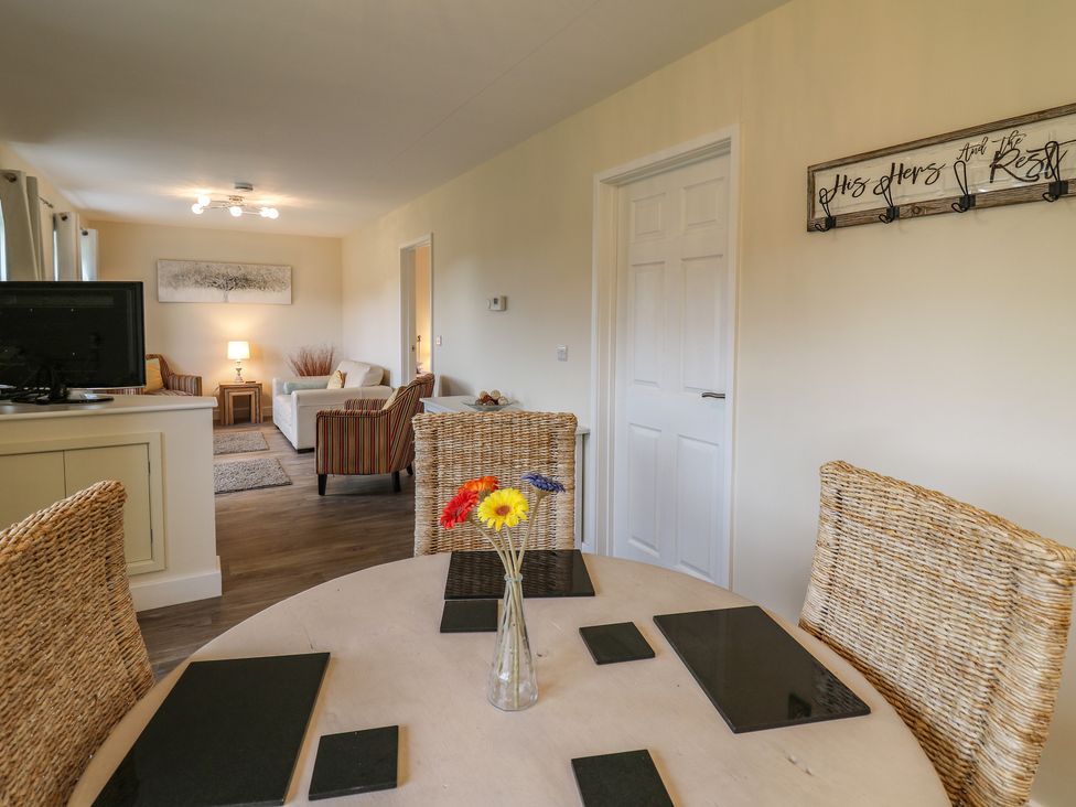 A dining table with black placemats and a vase with flowers and a living room with chairs and a lamp at Country Cottage in Brecon