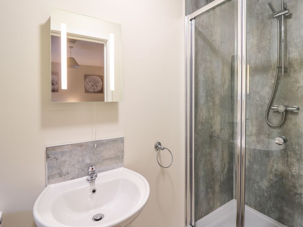 A bathroom with a sink and mirror next to a glass shower enclosure at Country Cottage in Brecon