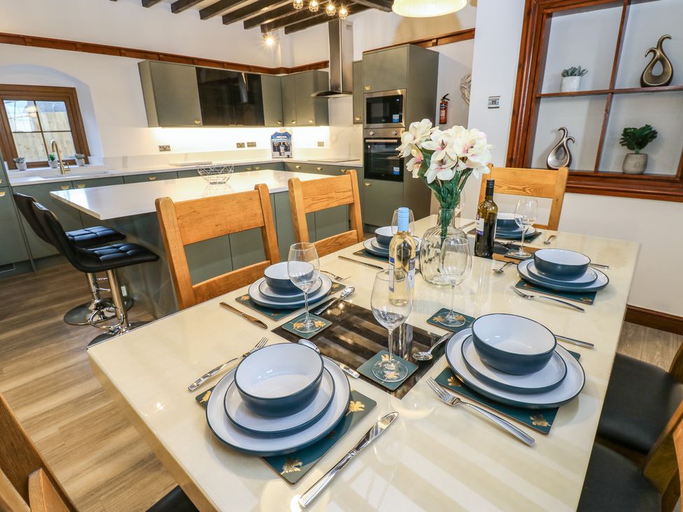 A dining table set with plates bowls glasses and cutlery in a kitchen with wooden chairs and gray cabinets at Winding Wheel Cottage in Cambois near Ashington