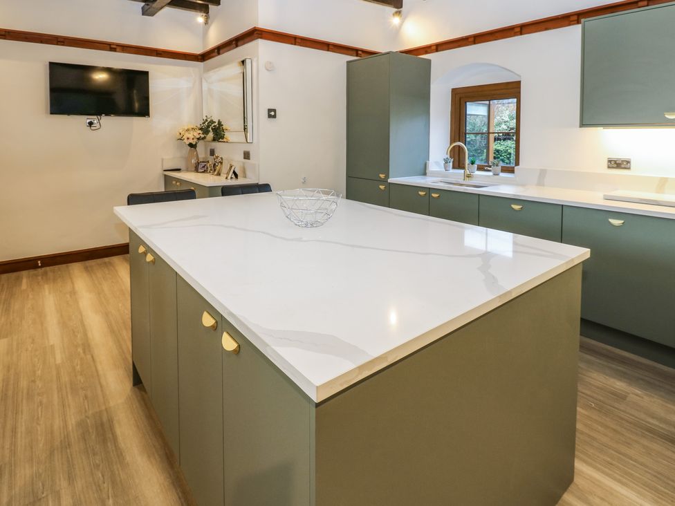 A kitchen with green cabinets a white countertop and a television on the wall at Winding Wheel Cottage in Cambois near Ashington