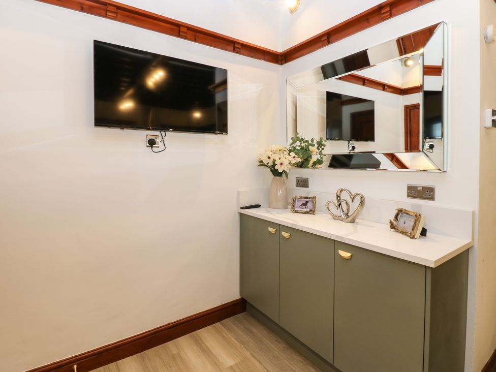 A wall-mounted television above a cabinet with a mirror flowers and decorative items at Winding Wheel Cottage in Cambois near Ashington