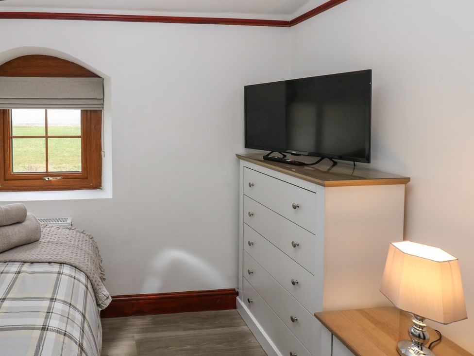 A bedroom corner with a window a chest of drawers with a TV on top and a lamp on a bedside table at Winding Wheel Cottage in Cambois near Ashington