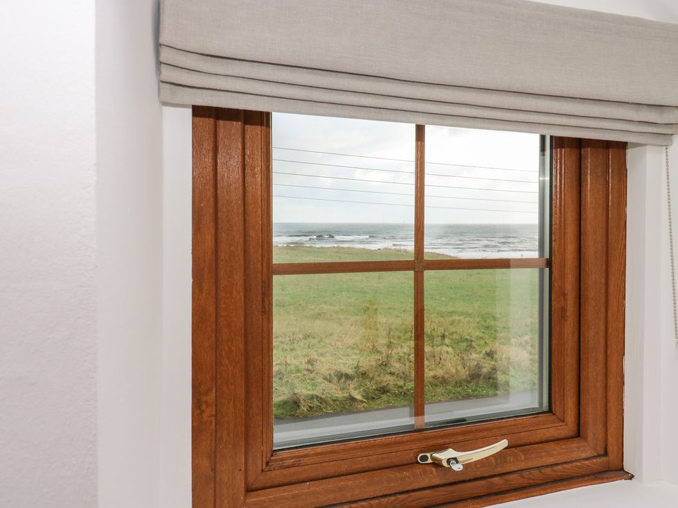 A wooden framed window with a beige blind showing a grassy field and sea beyond at Winding Wheel Cottage in Cambois near Ashington