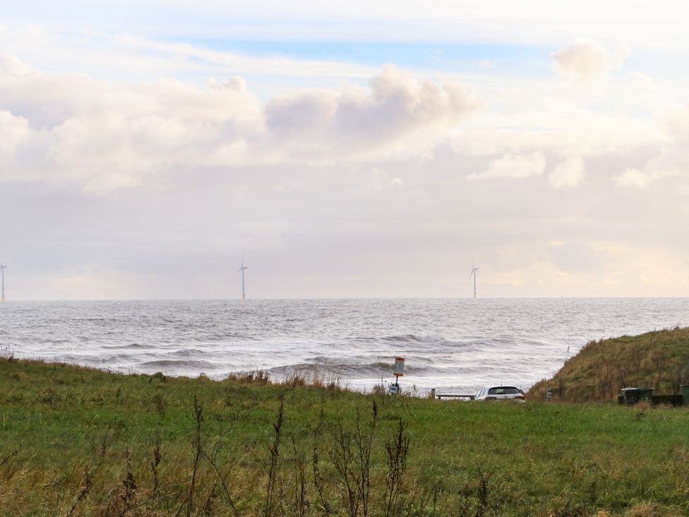 A grassy field with cars near a beach and wind turbines in the sea at Winding Wheel Cottage in Cambois near Ashington