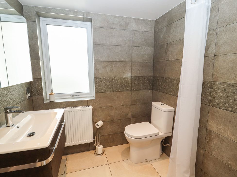 A bathroom with a toilet a sink a window and a shower curtain at Cherry Croft in Bowness-On-Solway