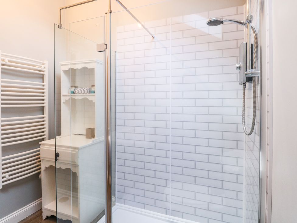 A bathroom with a walk in shower, white tiled wall, white storage cabinet, and a white towel radiator at The Grain Store in Haddiscoe