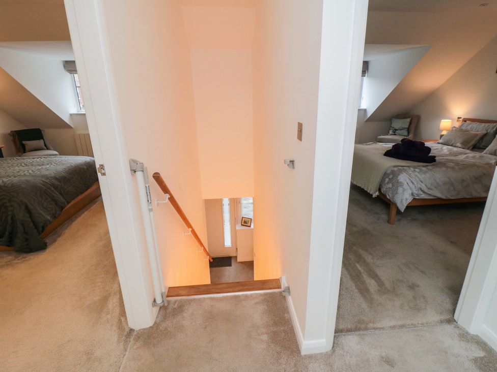 A hallway with stairs leading down between two bedrooms with beds and side tables at Martindale Cottage in Sleights