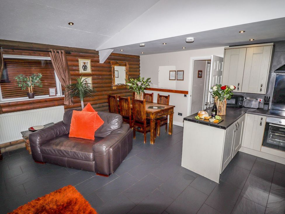 An open plan living area with a leather armchair and dining table next to a kitchen counter with flowers and bread at The Roe in Llanerch Park near St Asaph