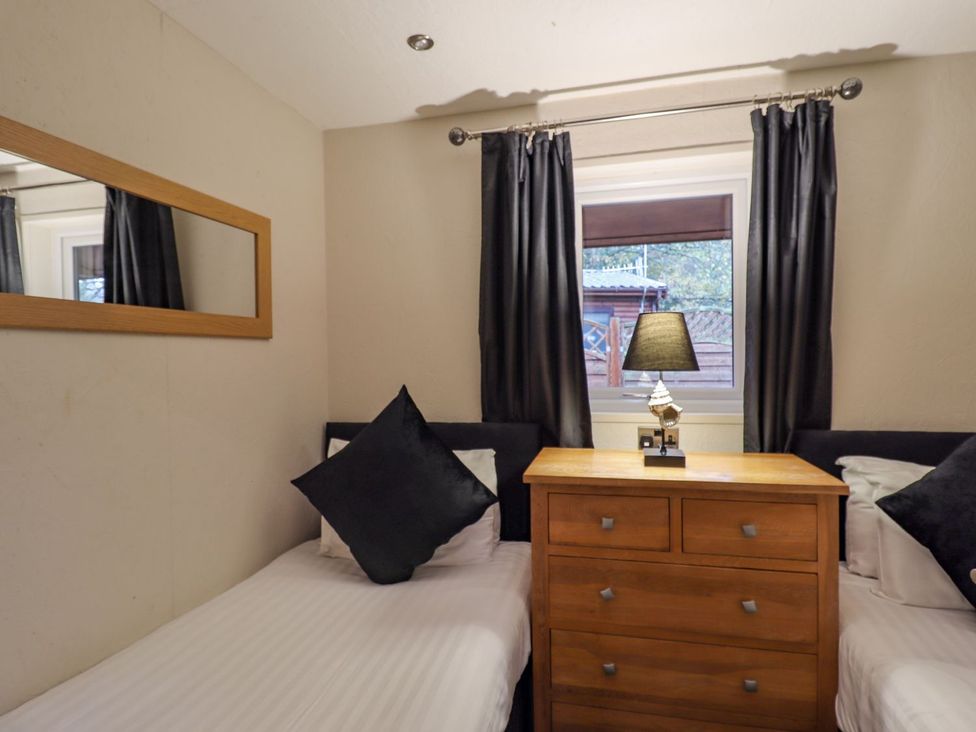 A bedroom with two single beds separated by a wooden chest of drawers and a window with black curtains at The Roe in Llanerch Park near St Asaph