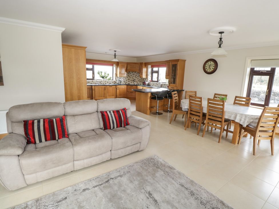 An open living area with a beige sofa with red striped cushions a wooden dining table with chairs and a kitchen with wooden cabinets and bar stools at Bunny Lane in Cloonflynn near Ballycarra County Mayo