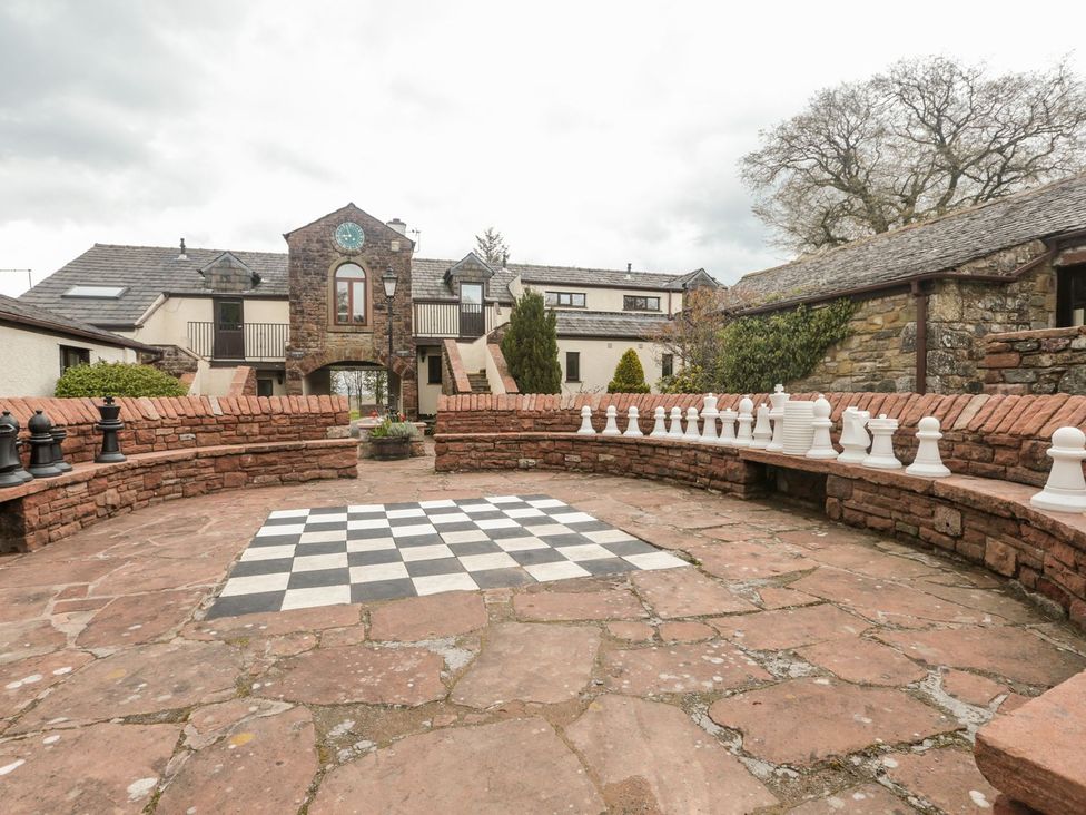 An outdoor patio area with a large chessboard painted on the ground and oversized chess pieces on stone benches at Squirrel Cottage in Penruddock