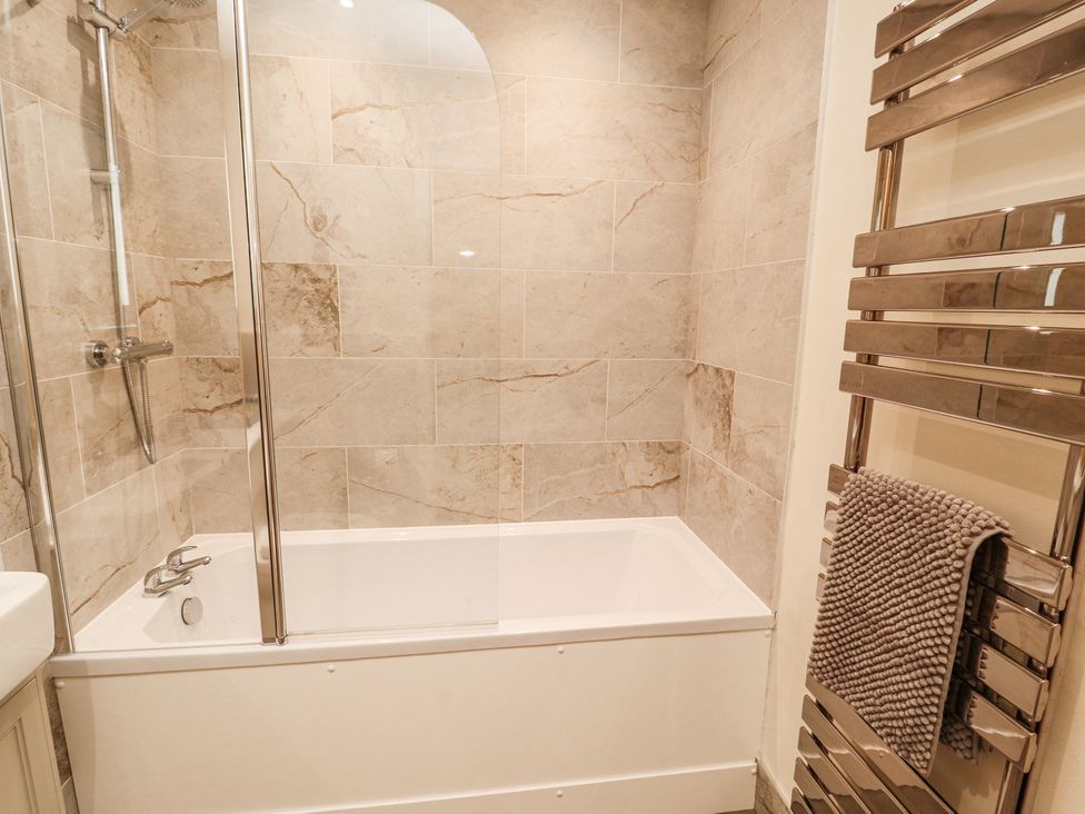 A bathroom with a bathtub shower combination tiled walls and a heated towel rail with a towel at Squirrel Cottage in Penruddock