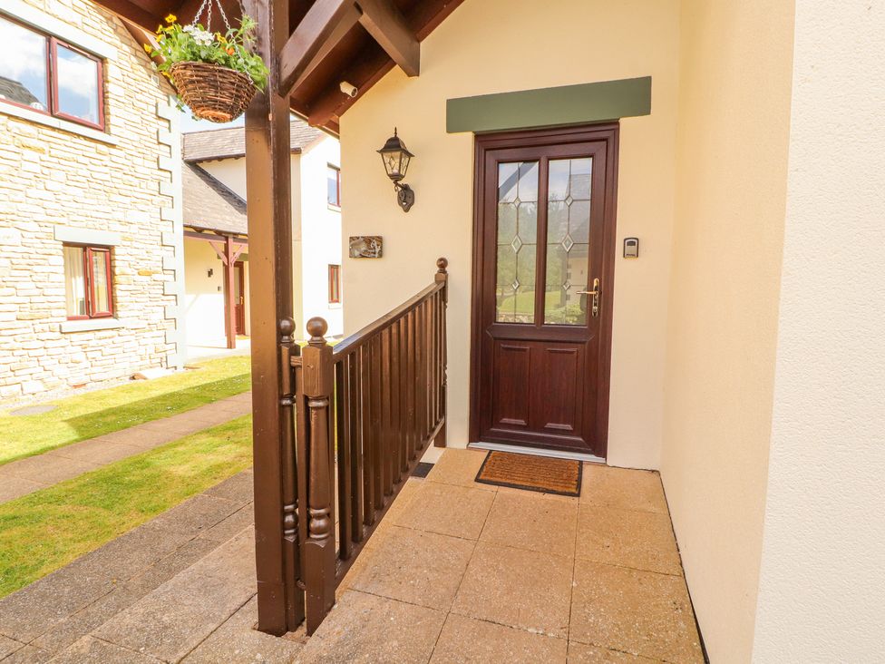 An entrance porch with a wooden door a hanging flower basket and a wooden railing at Squirrel Cottage in Penruddock