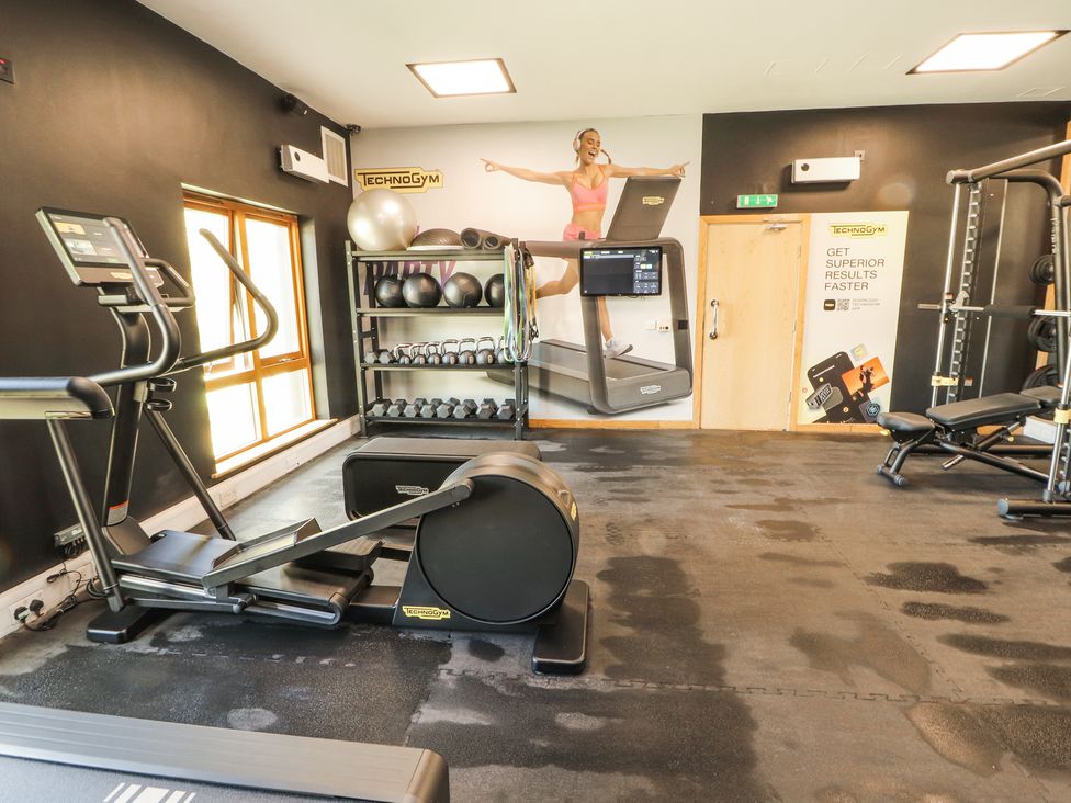 A gym room with exercise machines weights and a wall poster at Squirrel Cottage in Penruddock