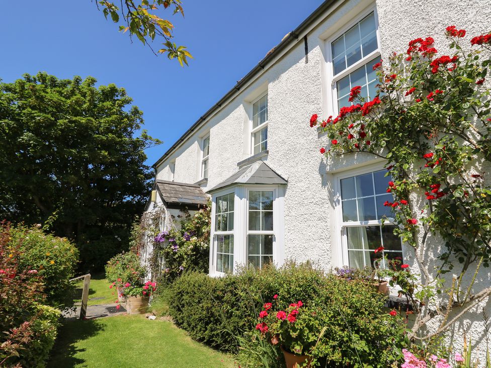 The exterior of a white house with multiple windows surrounded by flowers and bushes at Pen y Graig in Aberporth