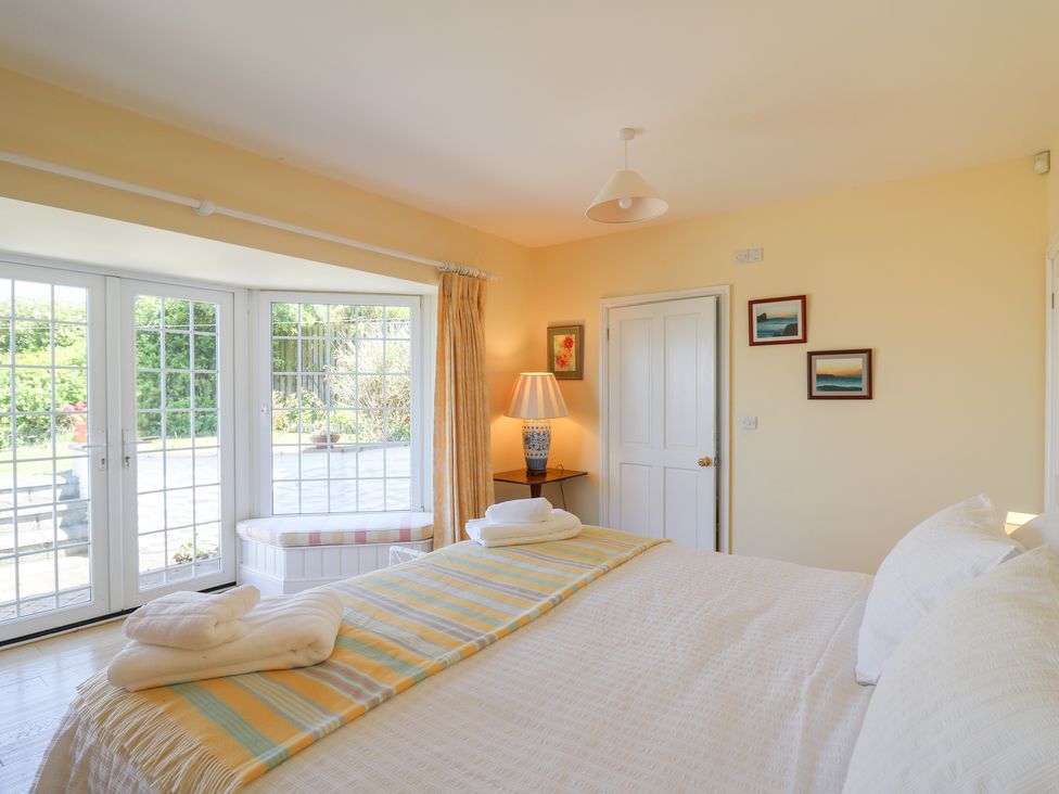 A bedroom with a bed towels on the bed and a window seat by glass doors at Pen y Graig in Aberporth