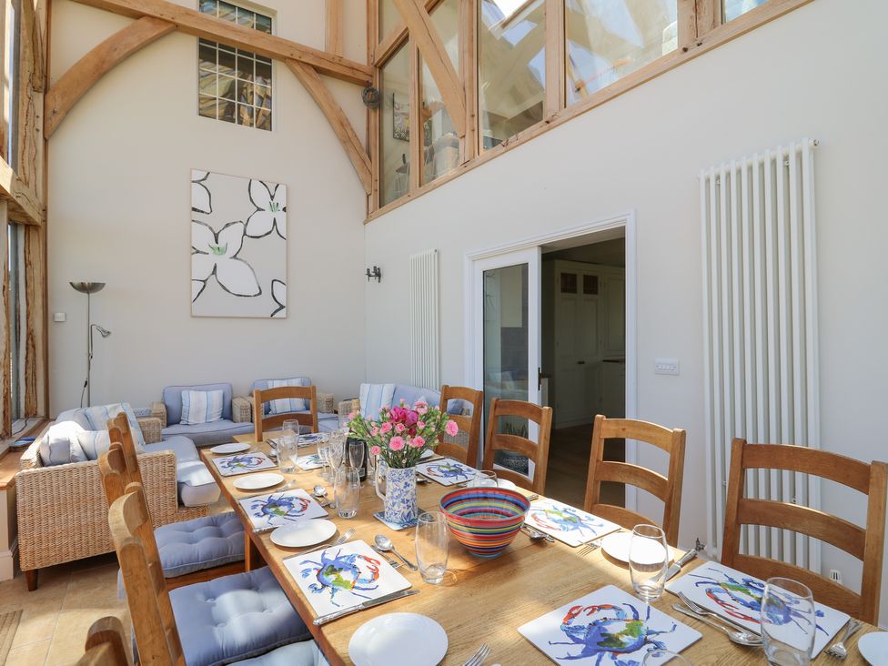 A dining room with a wooden table set with plates and crab-themed mats and a seating area with woven armchairs at Pen y Graig in Aberporth