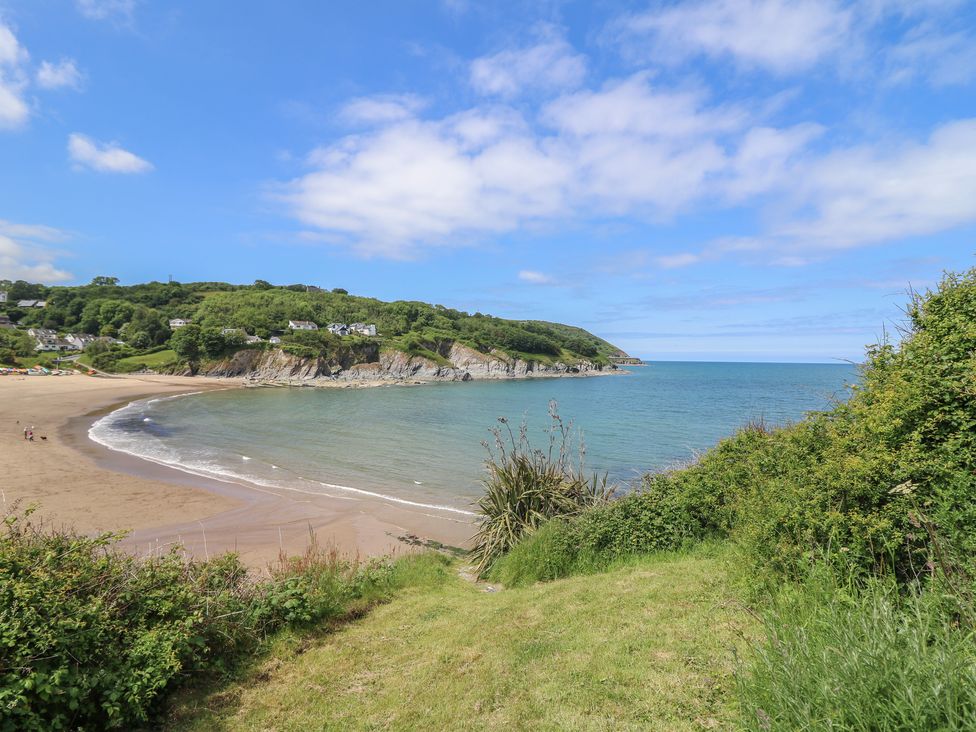 A view of a sandy beach with a curved shoreline and green hills with houses in the background at Pen y Graig in Aberporth