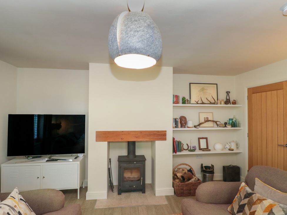 A living room with a wood stove fireplace tv on a cabinet and shelves with decorative items at Low Grounds Cottage Harome near Helmsley