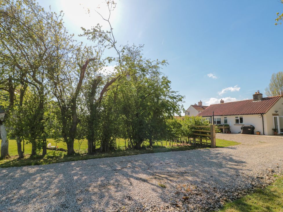 An outdoor scene with gravel driveway trees and a white house with a red roof at Low Grounds Cottage Harome near Helmsley