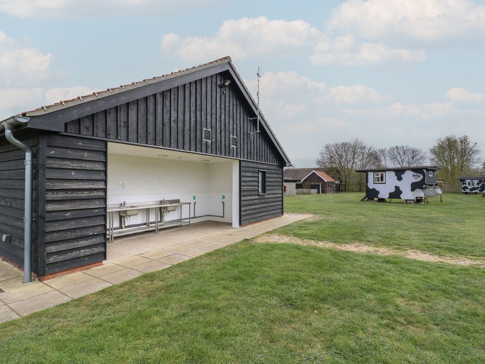 A black wooden shed with stainless steel sinks on a grassy field with cow-patterned huts at Daisy Cow Shed 1 in Easton near Campsea Ashe