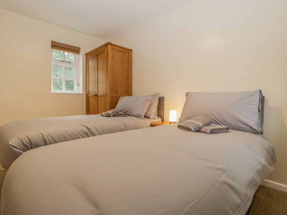 A bedroom with two single beds gray bedding wooden wardrobe and a small lamp on a nightstand at Heron's Lodge Llanover near Penperlleni