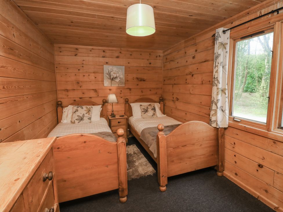 A bedroom with two wooden single beds a wooden chest of drawers and a window with floral curtains at Cedar in Dolton