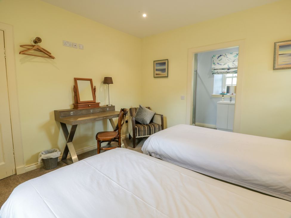 A bedroom with two beds a desk and chair a small armchair and a doorway to a bathroom at Kilnmark Farmhouse Auchenbrack near Moniaive