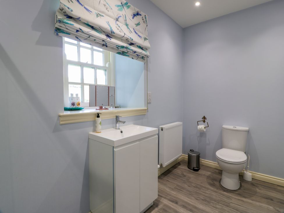 A bathroom with a sink cabinet a toilet a window with a patterned blind and a radiator at Kilnmark Farmhouse in Auchenbrack near Moniaive