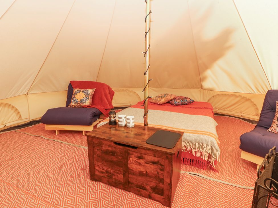 An interior of a tent with two cushioned chairs a bed with blankets a wooden chest and a pole with string lights at Kailzie in Peebles
