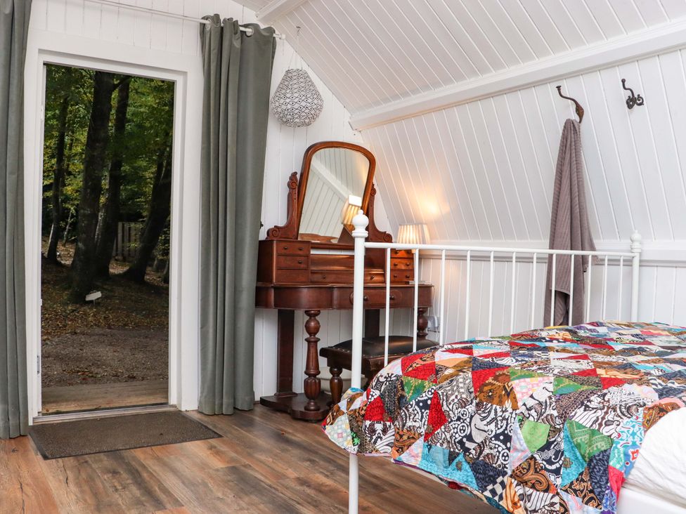A bedroom with a metal bed frame and a colorful patchwork quilt and a wooden dressing table with a mirror and a lamp at Ballybeg Pod 9 Ballybeg near Tinahely County Wicklow