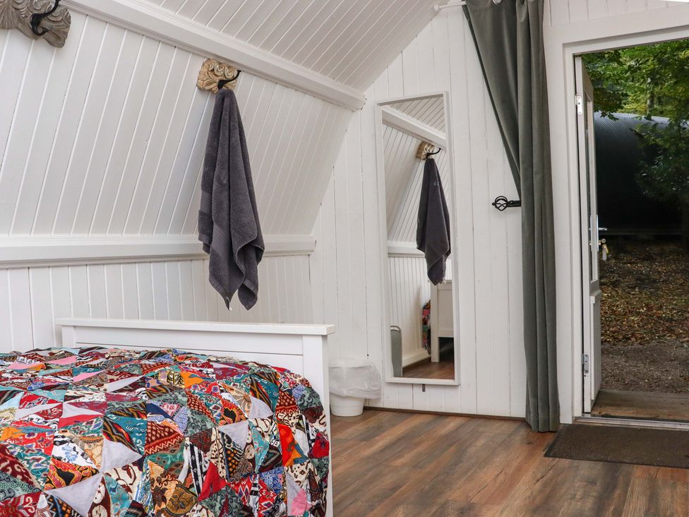 A bedroom with a patchwork quilt on a bed a gray towel hanging on the wall a full-length mirror and an open door leading outside at Ballybeg Pod 10 Ballybeg near Tinahely County Wicklow