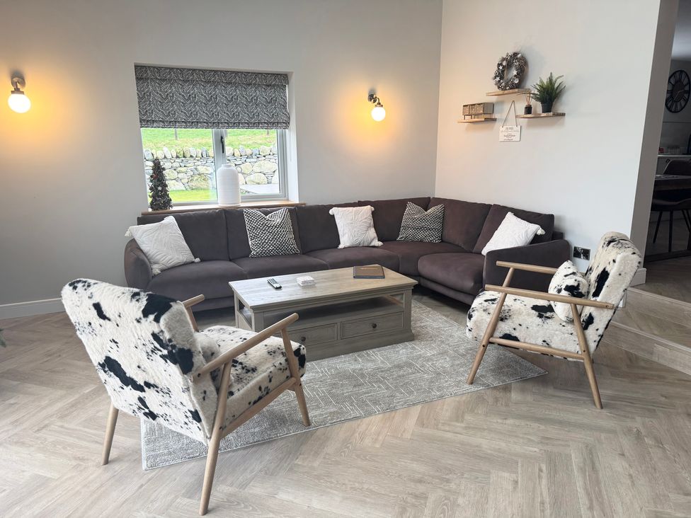 A living room with a brown sectional sofa, two patterned armchairs, a wooden coffee table, and a window with a patterned blind at Beudy Pwll Pridd in Llangollen