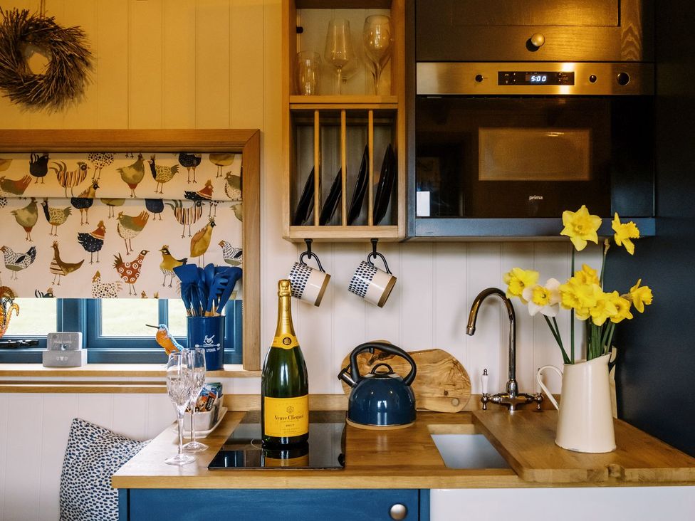 A kitchen counter with a bottle of champagne glasses kettle flowers and a microwave at Lillies Shepherds Hut at Shepherds Lodge Bottesford near Redmile and Vale of Belvoir