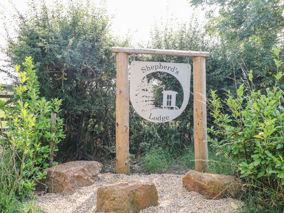 A wooden sign reading Shepherd's Lodge surrounded by bushes and rocks at Lillie's Shepherds Hut at Shepherds Lodge Bottesford near Redmile and Vale of Belvoir