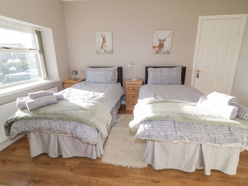 A bedroom with two single beds side by side two bedside tables with lamps animal paintings on the wall and towels on the beds at Ritas in Greencastle near Kilkeel