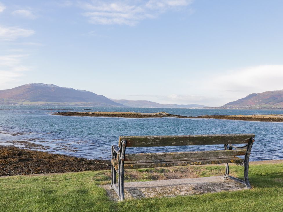 A wooden bench on grass facing a body of water with hills in the background at Ritas Greencastle near Kilkeel