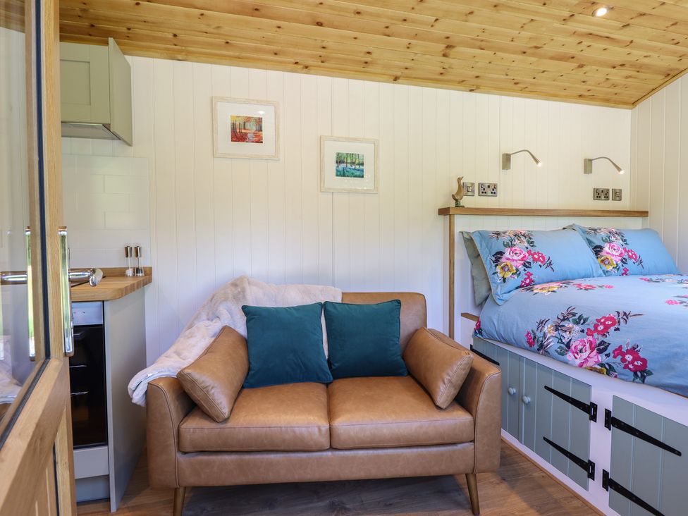 A small room with a brown leather sofa with blue cushions beside a bed with blue floral bedding at Celyn in Bontddu near Dolgellau