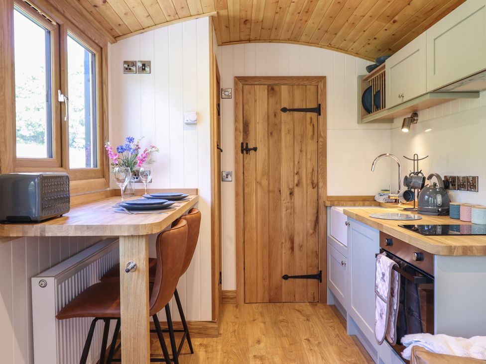 A kitchen with wooden countertops, brown chairs at a breakfast bar, a wooden door, and kitchen appliances at Celyn in Bontddu near Dolgellau